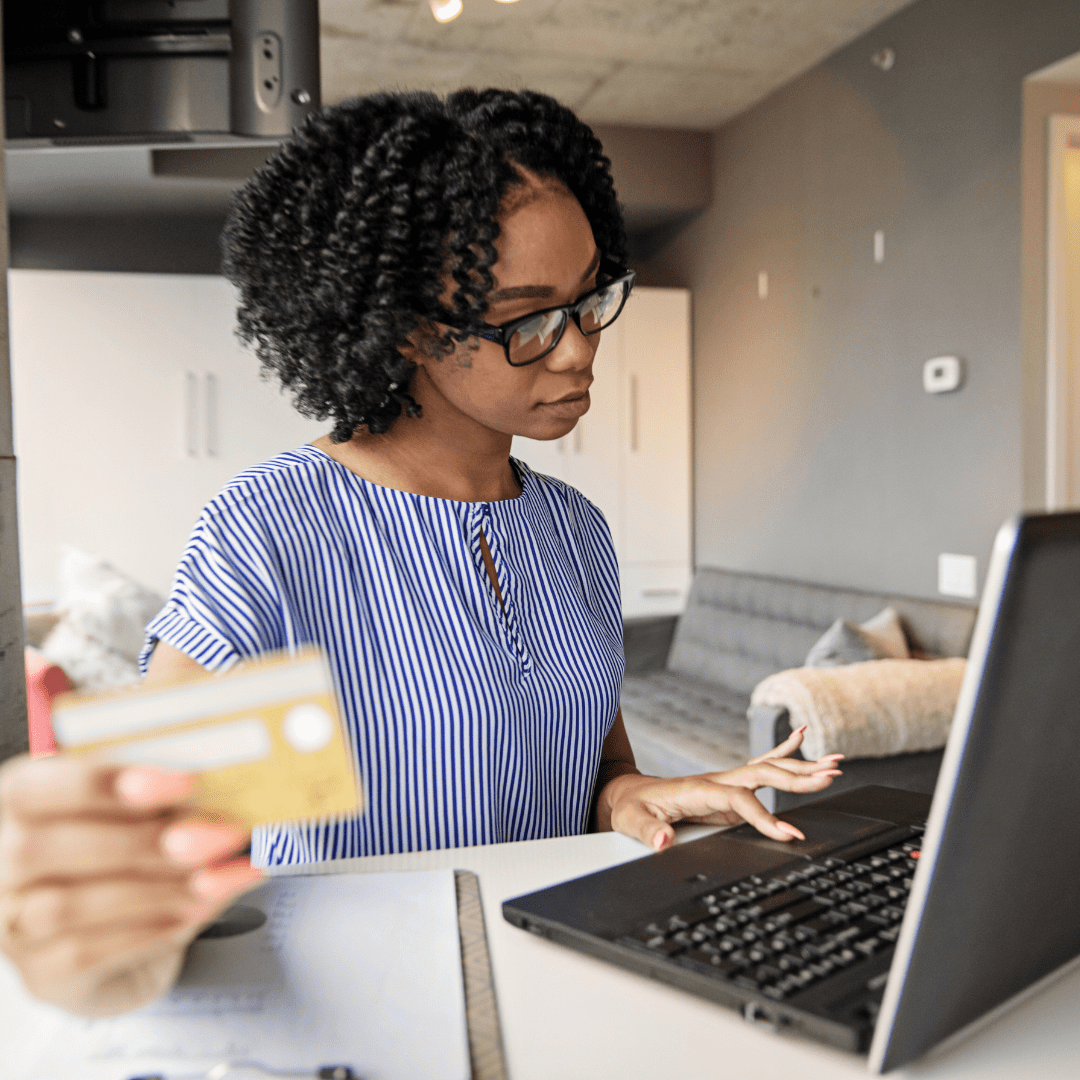 "Smiling woman shopping online with a credit card while using a laptop at home."